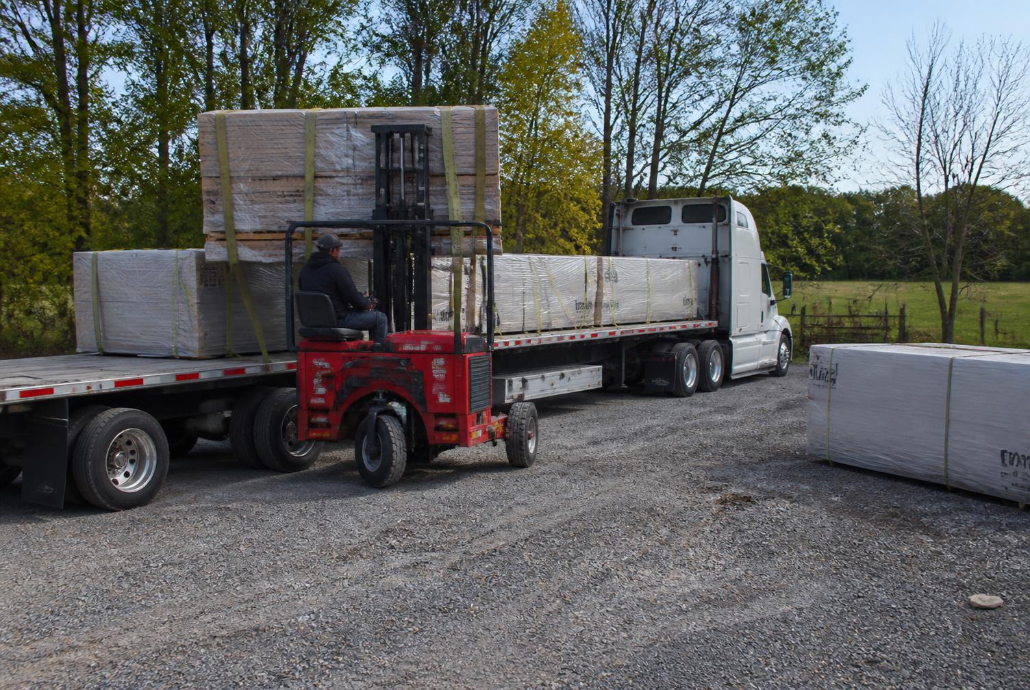 Semi trailer with a piggyback forklift unloading bundled building materials on a gravel lot